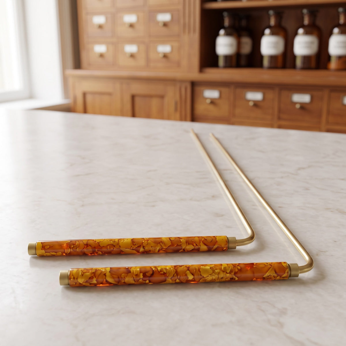 Zwei Wünschelruten 22 cm mit orange marmorierten Griffen liegen schräg von vorn auf der Marmortheke einer hellen Apotheke