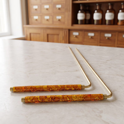 Zwei Wünschelruten 22 cm mit orange marmorierten Griffen liegen schräg von vorn auf der Marmortheke einer hellen Apotheke