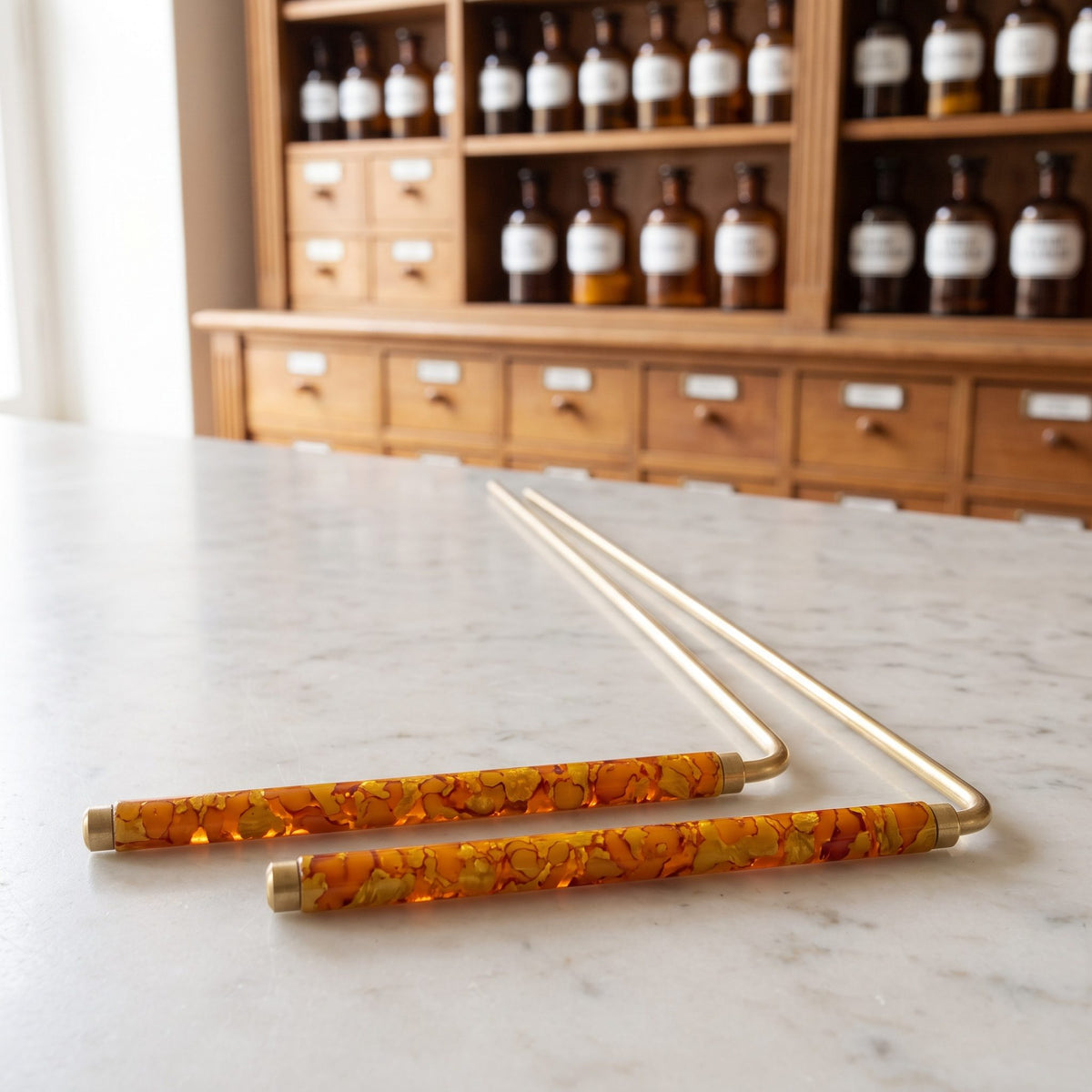 Zwei Wünschelruten 34 cm mit orange marmorierten Griffen liegen schräg von vorn auf der Marmortheke einer hellen Apotheke