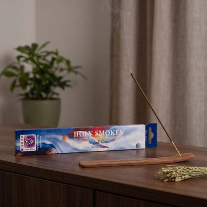 Nepali Gras Räucherstäbchen Holy Smokes Blue Line: glimmendes Räucherstäbchen mit feinem Rauch im Holzhalter, dahinter die Packung, auf einem Sideboard am Abend