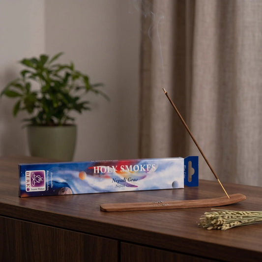 Nepali Gras Räucherstäbchen Holy Smokes Blue Line: glimmendes Räucherstäbchen mit feinem Rauch im Holzhalter, dahinter die Packung, auf einem Sideboard am Abend