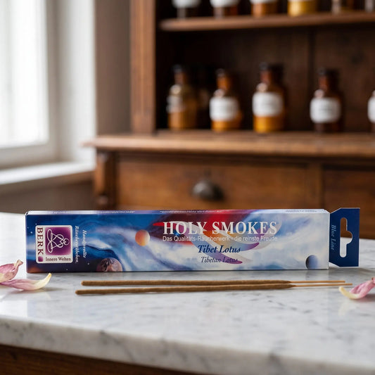 Tibet Lotus Räucherstäbchen Blue Line: Packung auf einer Marmortheke vor einem Apothekerschrank, daneben zwei lose Räucherstäbchen und ein paar getrocknete Lotusblütenblätter – Spirit of Gaia