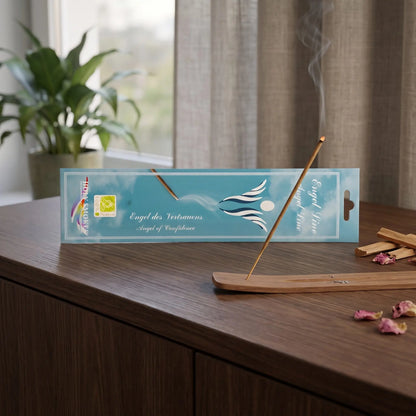 Engel des Vertrauens Räucherstäbchen Holy Smokes: glimmendes Räucherstäbchen mit feinem Rauch im Holzhalter, dahinter die Packung, auf einem Sideboard am Abend