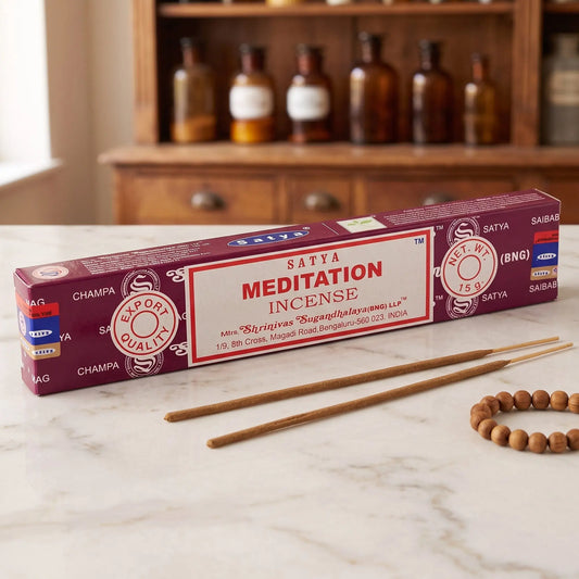 Satya Meditation Räucherstäbchen: 15-g-Packung auf einer Marmortheke vor einem Apothekerschrank, daneben zwei lose Räucherstäbchen – Spirit of Gaia