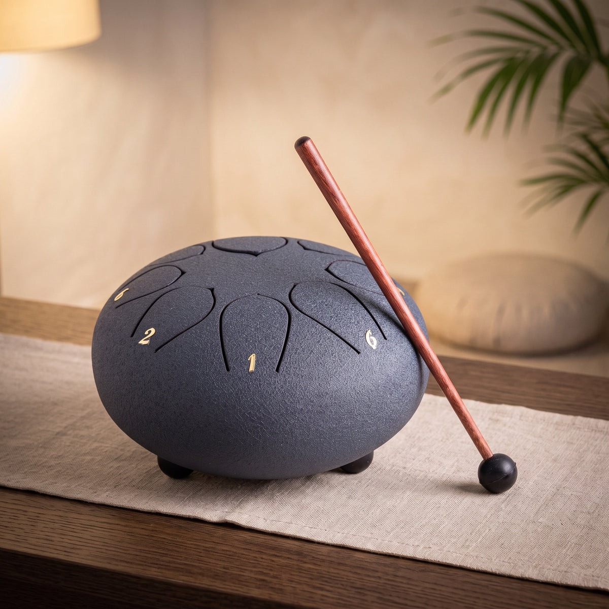 Mittlere dunkelblaue Steeldrum mit Klangstab auf einem Leinenläufer, dahinter ein warmer Meditationsraum