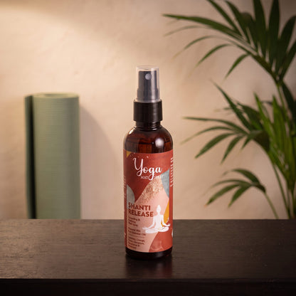 Yogamatten-Spray Shanti Release von Song of India, 100 ml, auf einer dunklen Holzbank in einem Meditationsraum, dahinter eine aufgerollte Yogamatte