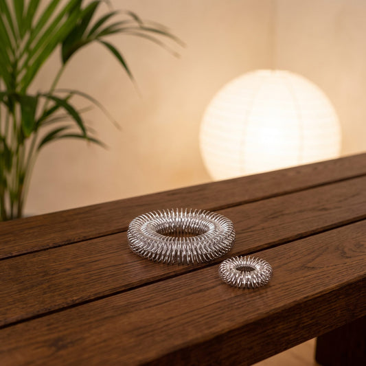 Akupressur-Massage-Set, Reflexringe für Finger, Hand und Arm: großer und kleiner Ring aus silbernem Federdraht auf einer Holzbank im Meditationsraum am Abend – Spirit of Gaia