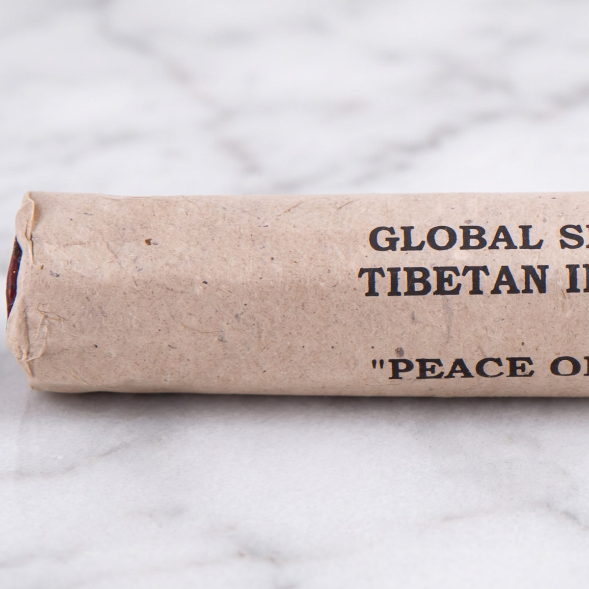 Nahaufnahme der Papierrolle Frieden des Geistes (Peace of Mind) mit der Aufschrift Global Shaman Tibetan Incense und den roten Stäbchenenden auf Marmor