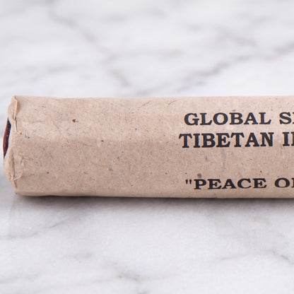 Nahaufnahme der Papierrolle Frieden des Geistes (Peace of Mind) mit der Aufschrift Global Shaman Tibetan Incense und den roten Stäbchenenden auf Marmor