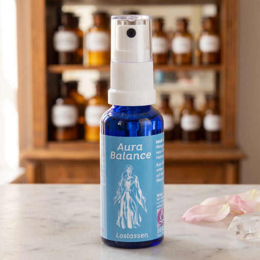 Energiespray Loslassen (Aura Balance): blaue Sprühflasche mit hellblauem Etikett auf Marmortheke vor Apothekerschrank, daneben ein Bergkristall und Rosenblütenblätter – Spirit of Gaia